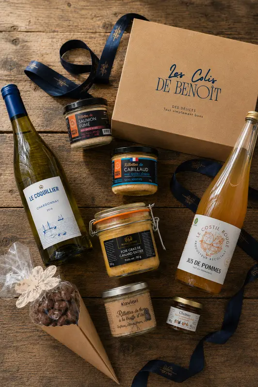 Coffret gourmand ouvert : vin blanc, jus de pomme, terrines et douceurs sur une table en bois